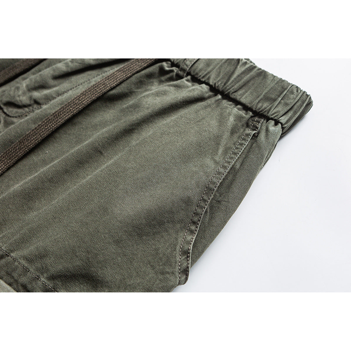Close-up of olive pants showing the elastic waistband, drawcord, and stitched side seam.