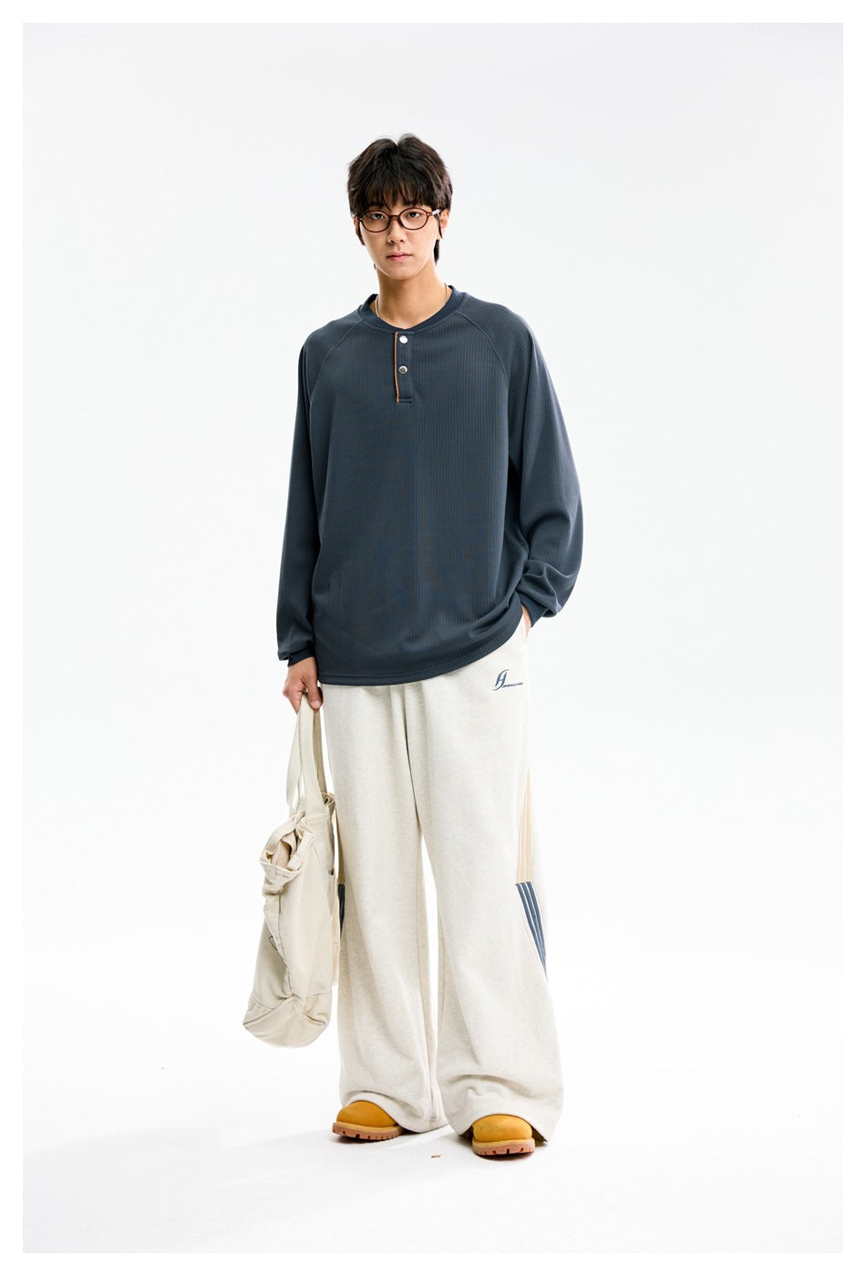 Model wearing a blue ribbed henley top with off-white wide-leg sweatpants and holding a cream tote bag