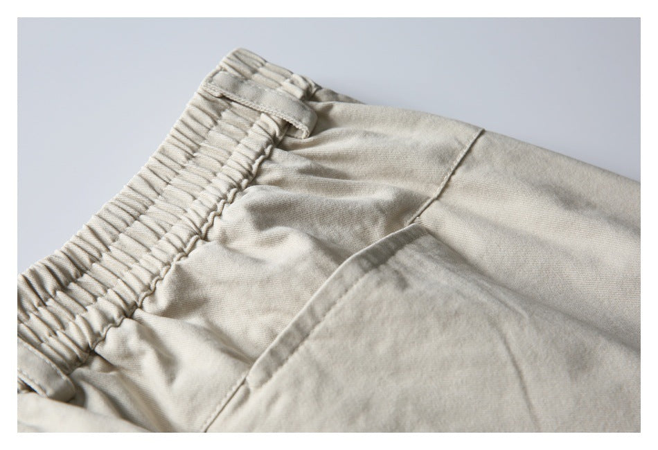 Close-up of pale beige trousers showing a gathered elastic waistband, belt loop, seams, and pocket.