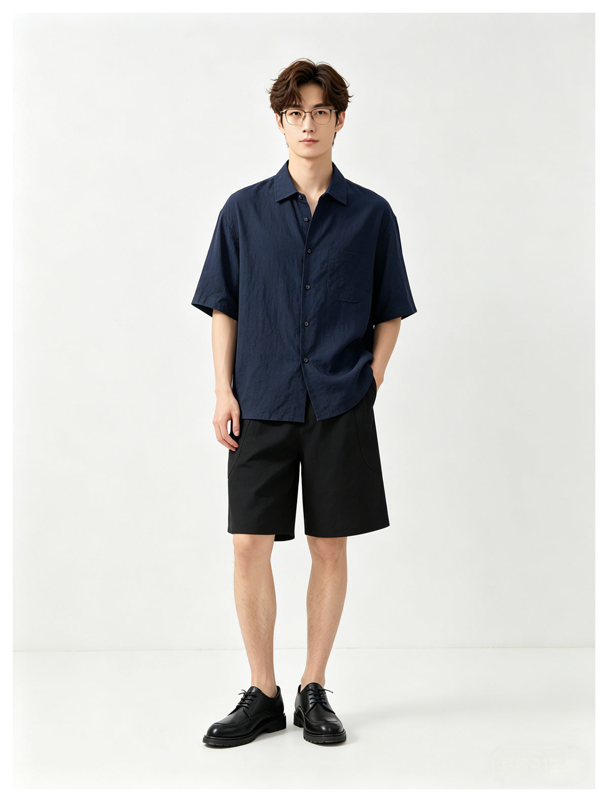 Model wearing a navy short-sleeve button-up shirt with a chest pocket and black shorts, facing forward.