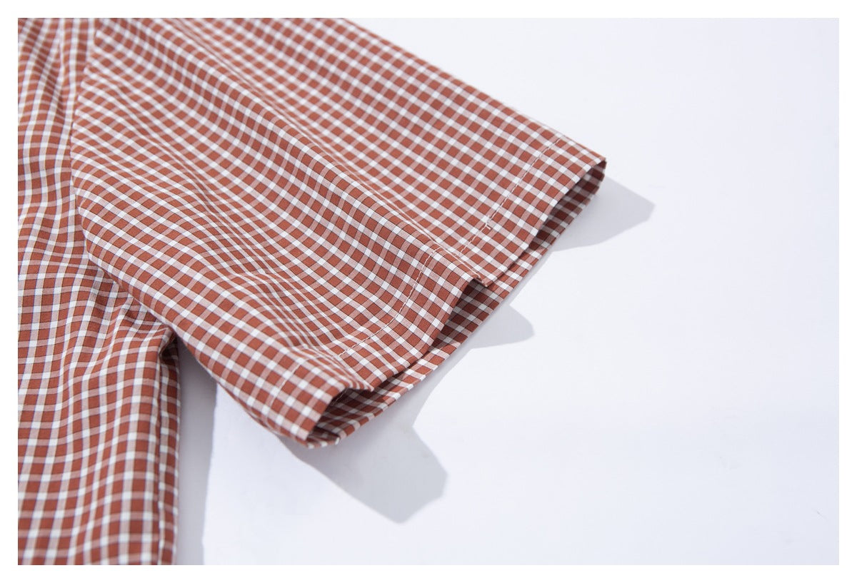 Close-up of the short sleeve and stitched cuff on a rust-brown and white gingham shirt.