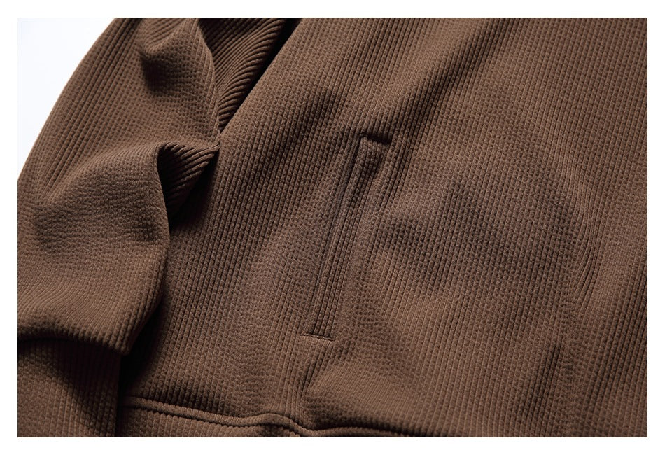 Close-up of the brown hoodie’s textured fabric and vertical opening of the front kangaroo pocket.