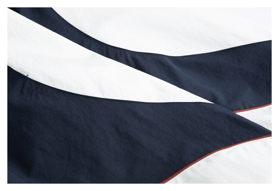 Close-up of white and navy color-blocked garment panels with narrow burgundy piping.