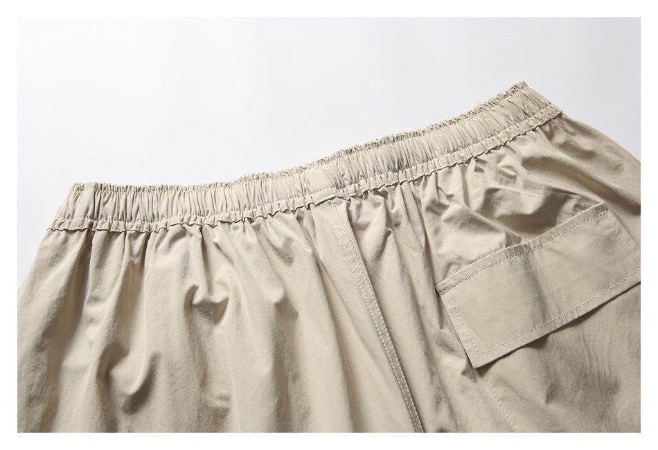 Close-up of beige shorts showing the gathered elastic waistband, center seam and large side pocket.