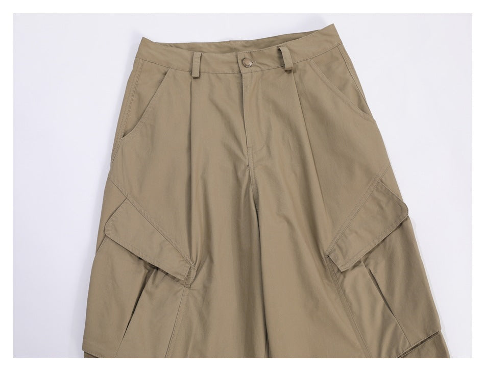 Close-up of the upper front of tan cargo trousers, showing the waistband, angled pockets and large layered side pockets.