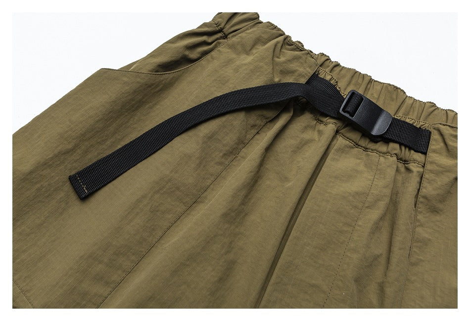 Close-up of olive pants with an elastic waistband and a long black webbing strap fastened by a buckle.