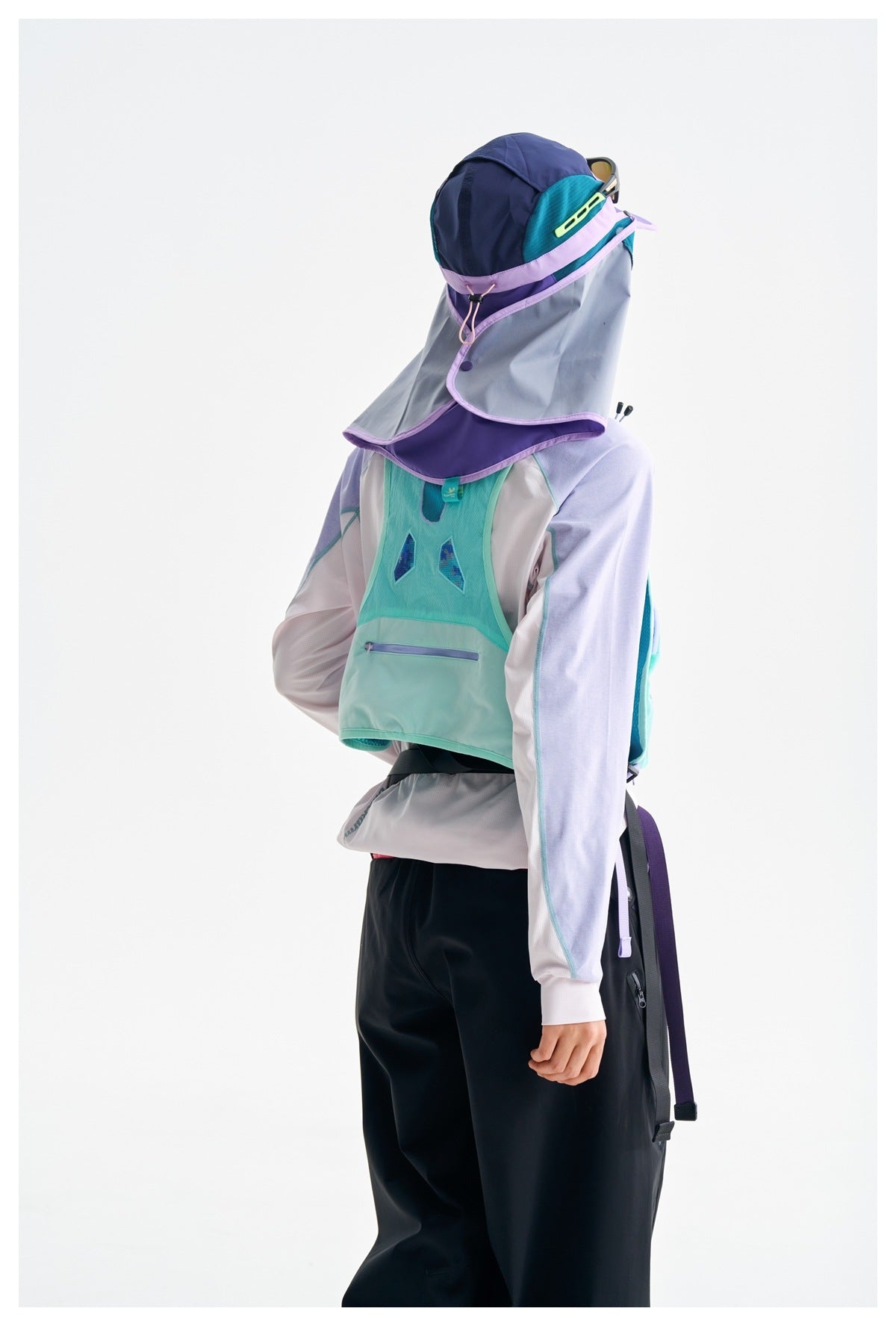 Person wearing a navy, teal and purple sun hood with face drape, a pastel top and black pants.