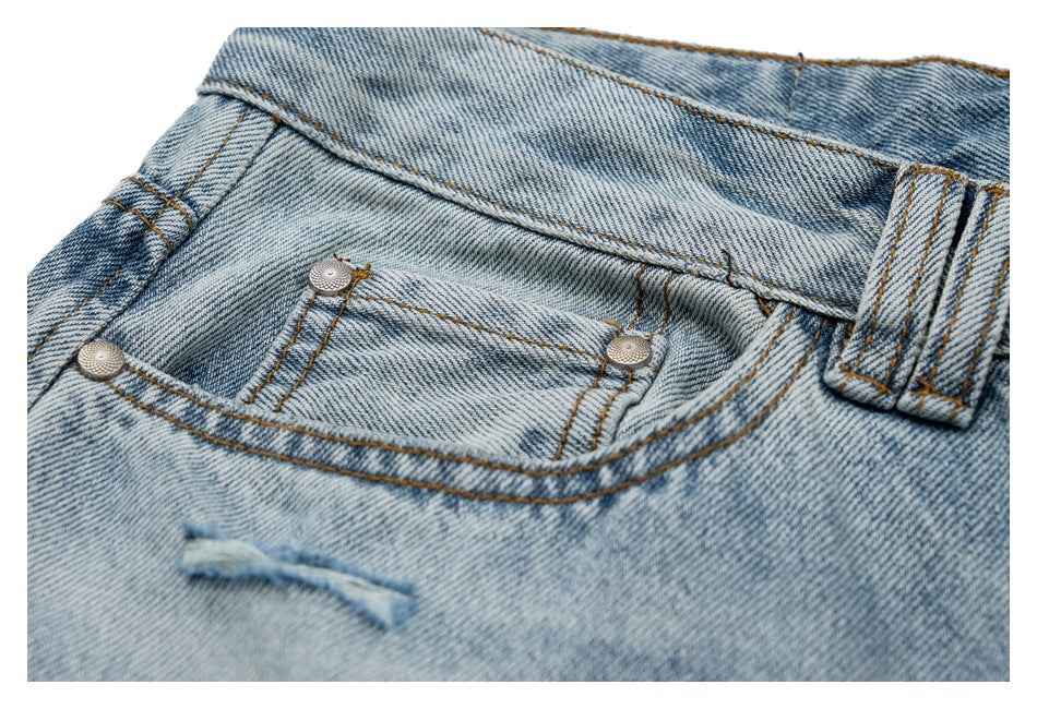 Close-up of light blue jeans showing a front pocket, metal rivets, belt loop, and small frayed tear.