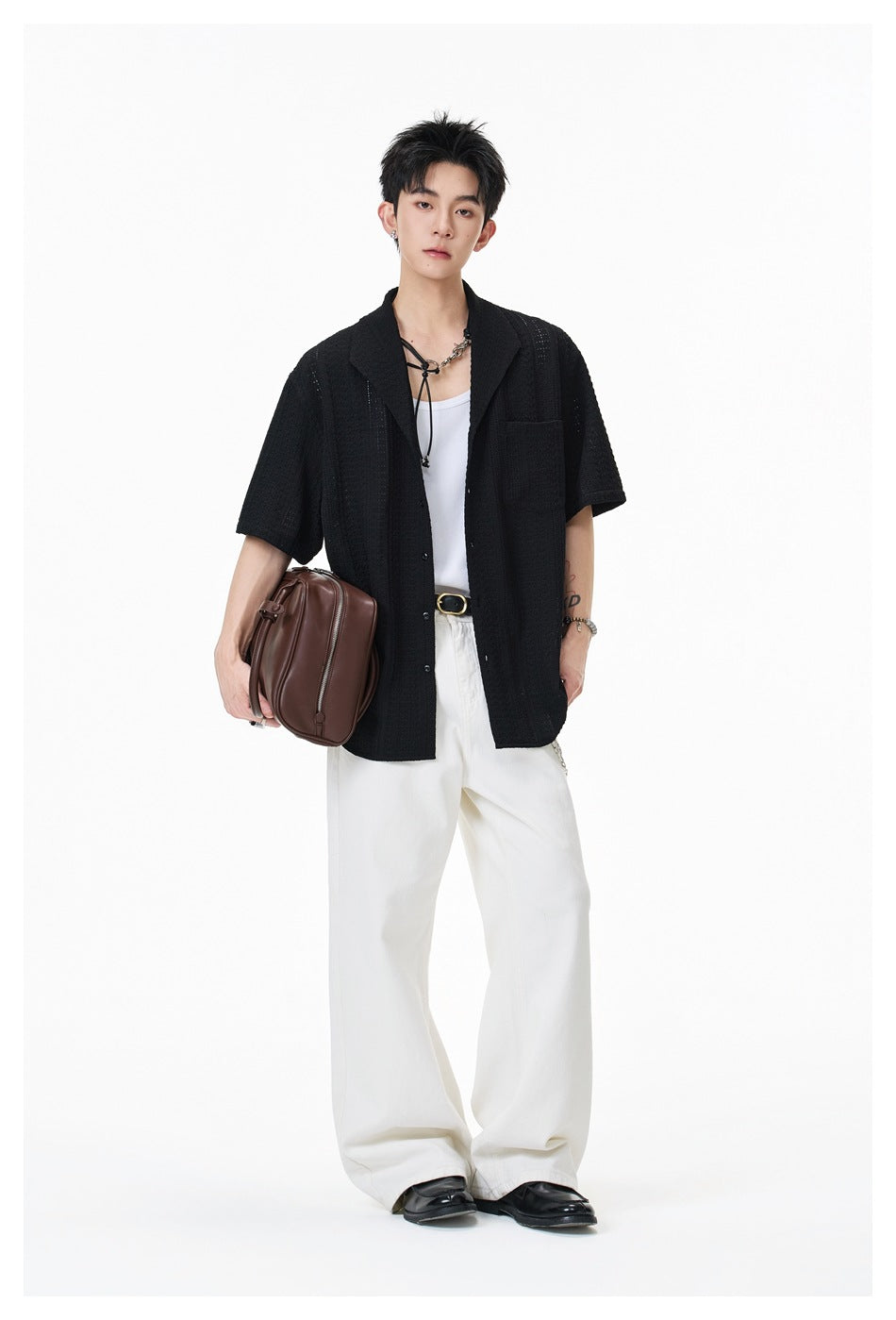 Model wearing black textured short-sleeve shirt open over a white tank top with white wide-leg pants and brown bag