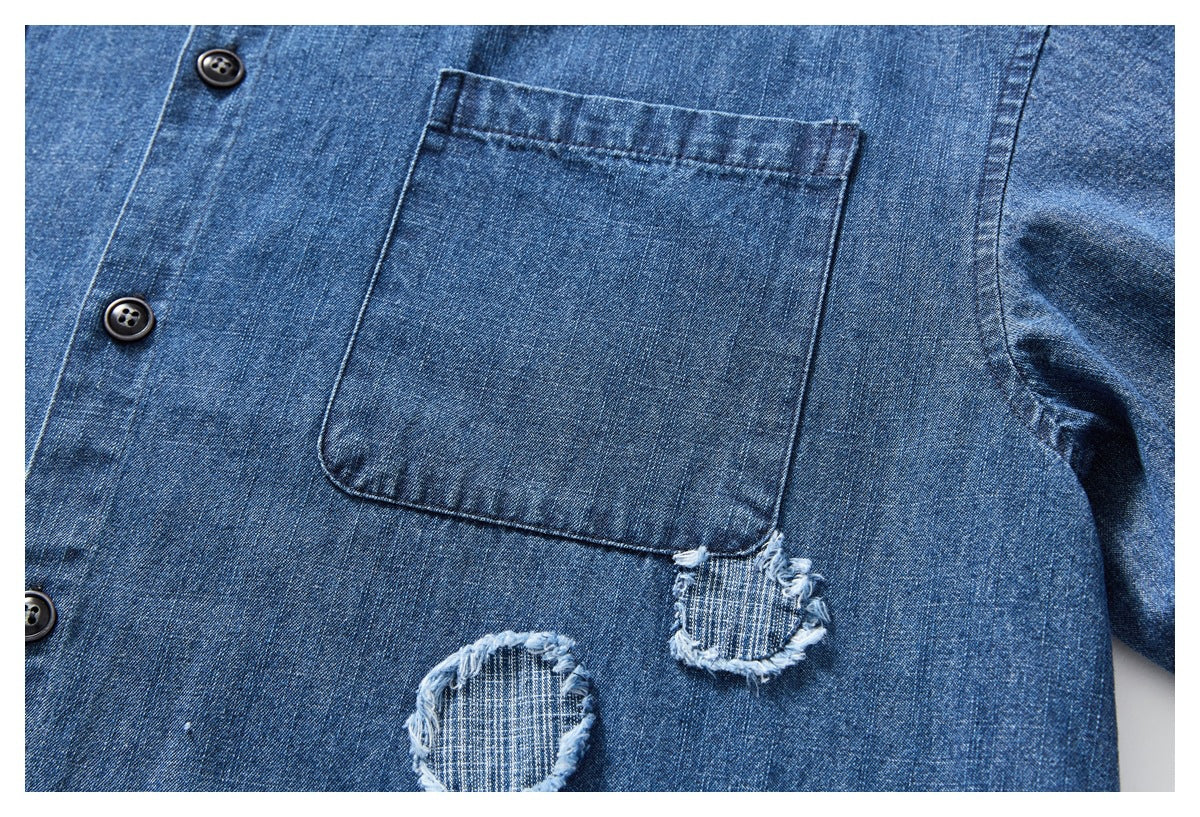 Close-up of a blue denim shirt pocket, black buttons, and frayed distressed patches.