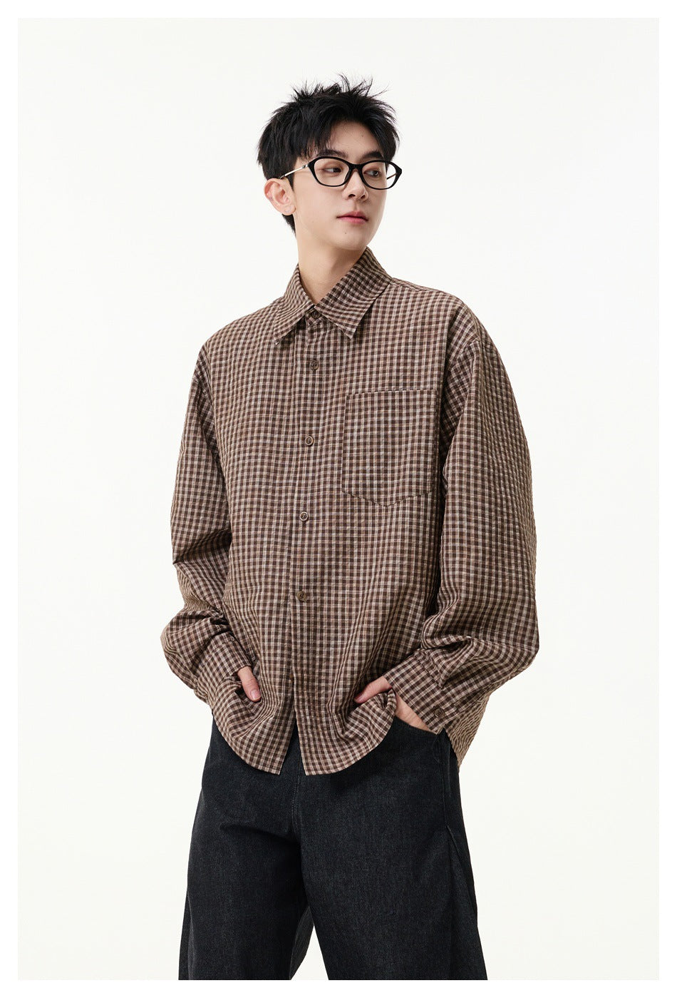 Model wearing a brown checked button-up shirt with a chest pocket and dark wide-leg trousers.