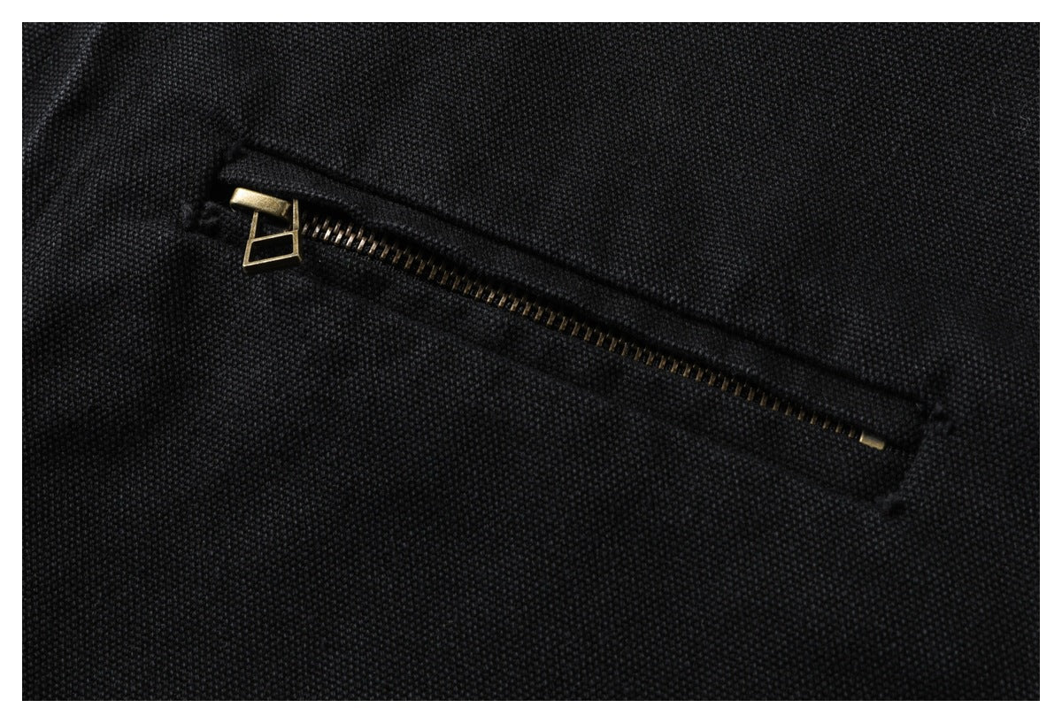 Close-up of a diagonal zip pocket on black textured fabric, with a brass-tone zipper.