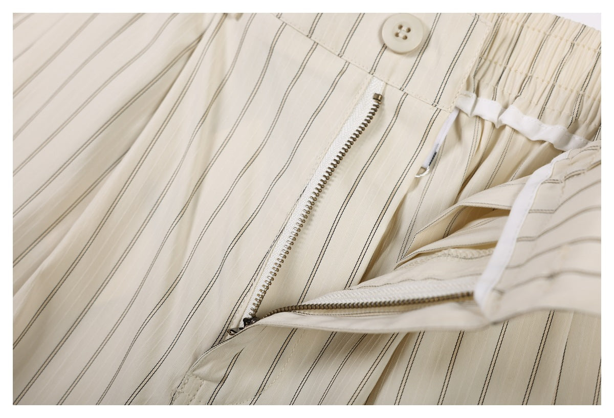 Close-up of a button and metal zipper at the waist of cream trousers with thin dark stripes.