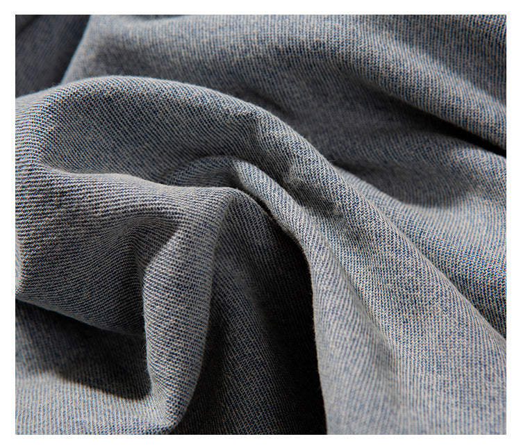 Macro view of light blue denim fabric gathered into folds, showing its diagonal weave.