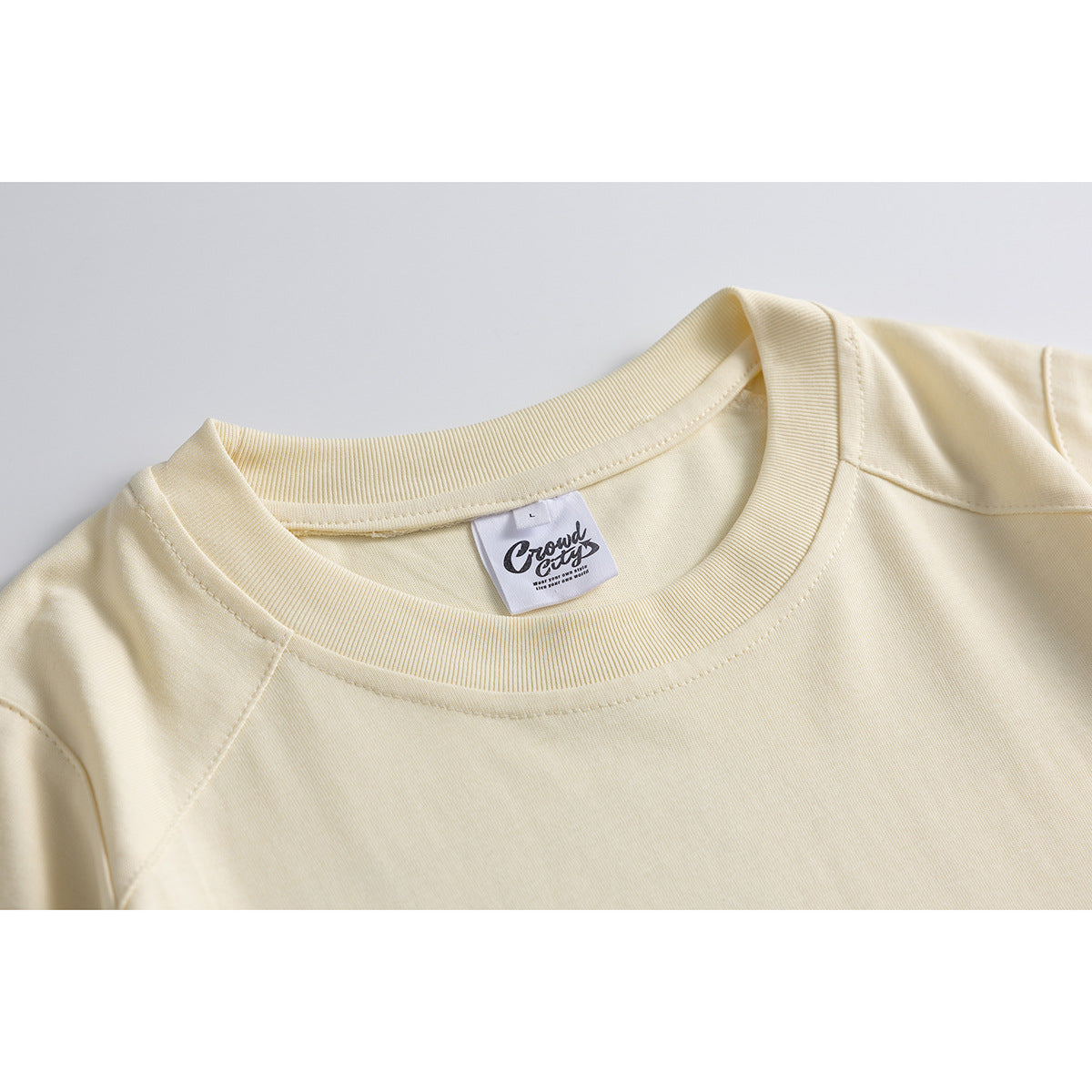 Close-up of a cream T-shirt's ribbed crew neck, shoulder seams, and inner label.