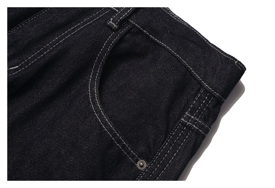 Close-up of a curved front pocket and reinforced side seam on black denim jeans.