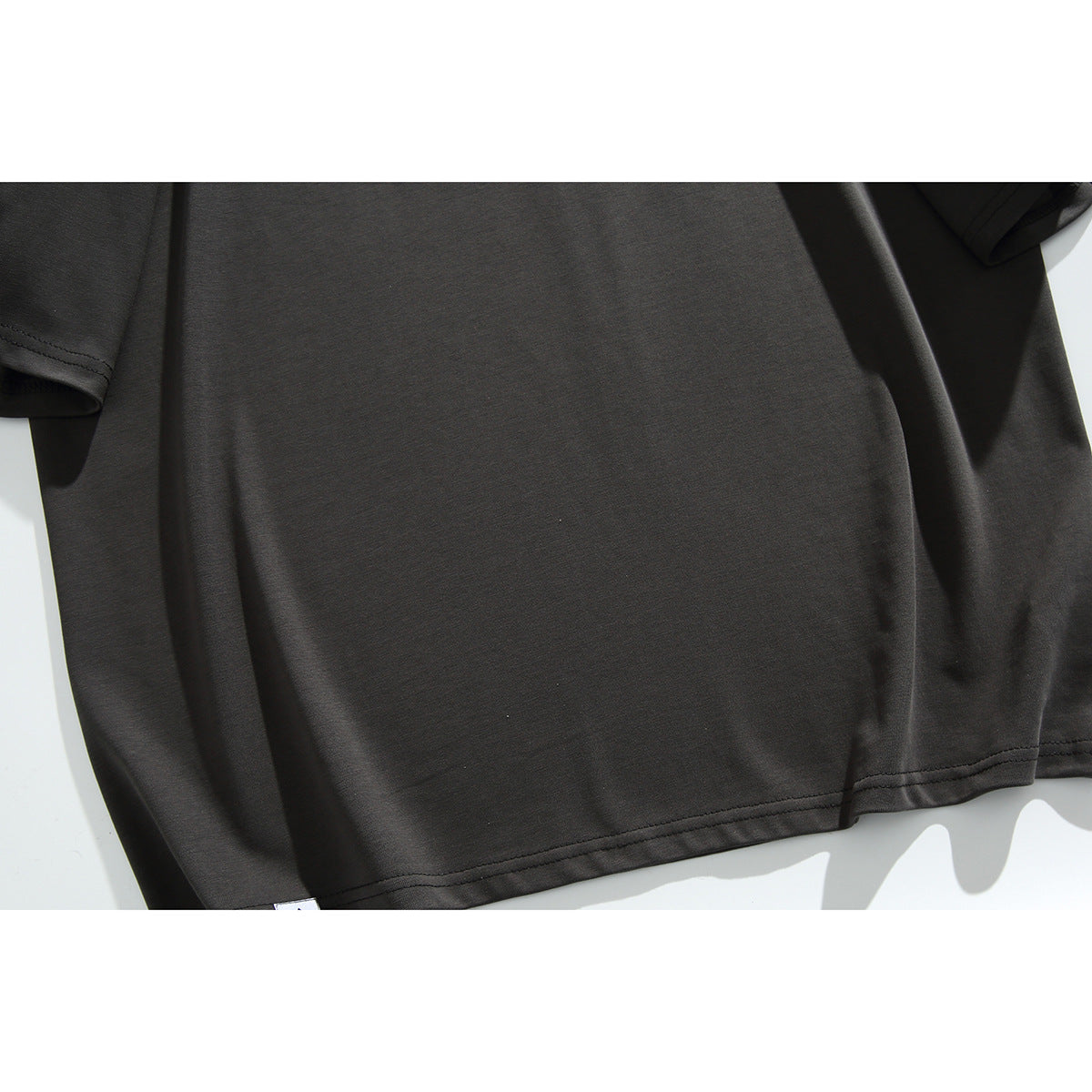 Close-up of the plain charcoal back of a short-sleeve T-shirt, showing its hem and sleeve seams.