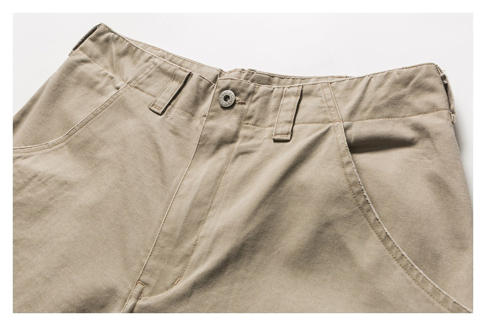 Close-up of beige trousers showing the front waistband, belt loops, button, fly and curved pocket openings.