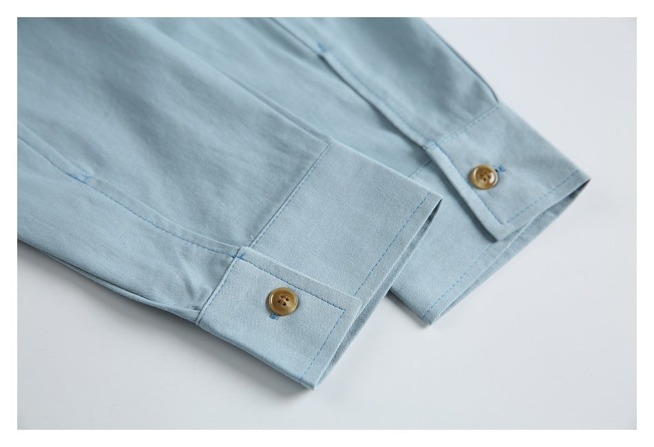 Close-up of a pale blue shirt sleeve and cuffs with tan buttons.