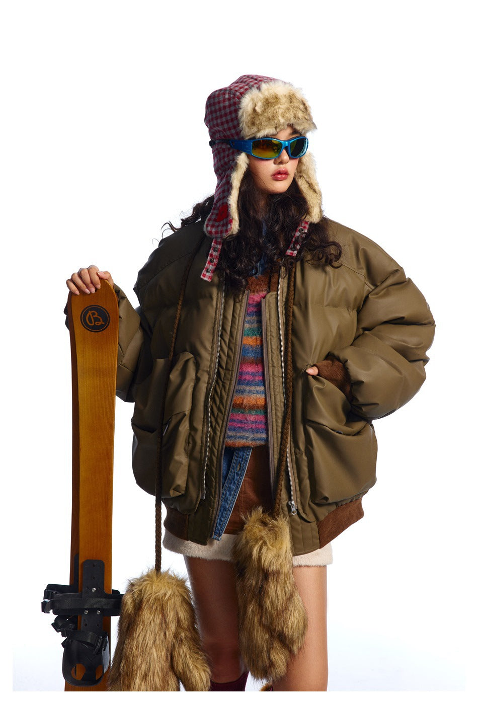 Model in an oversized olive-brown padded bomber jacket with large pockets and brown ribbed trim, viewed from the front.