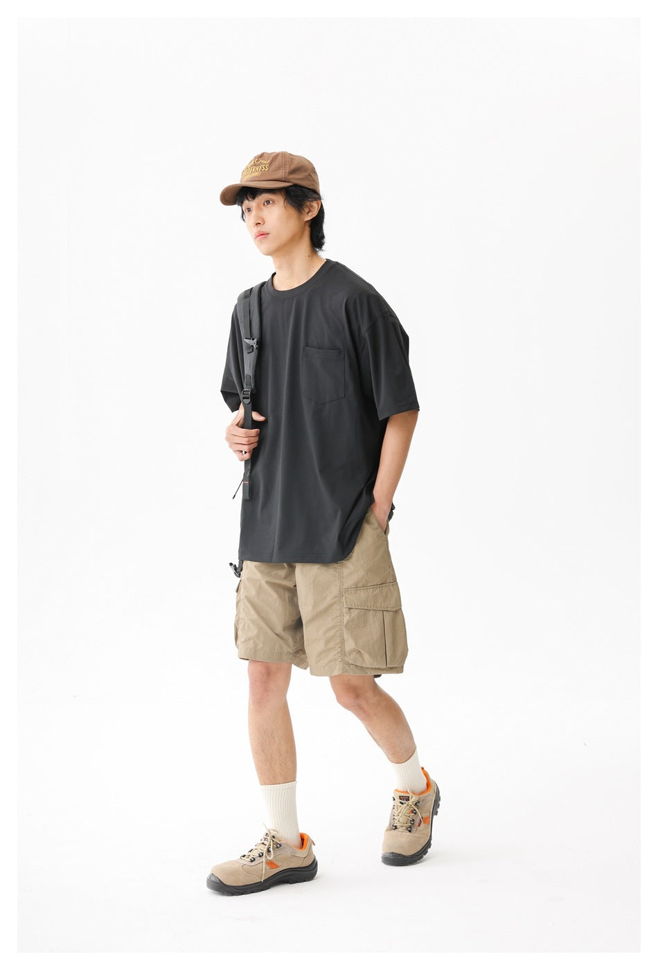 Three-quarter view of a model in a black pocket T-shirt and tan cargo shorts with a backpack strap.