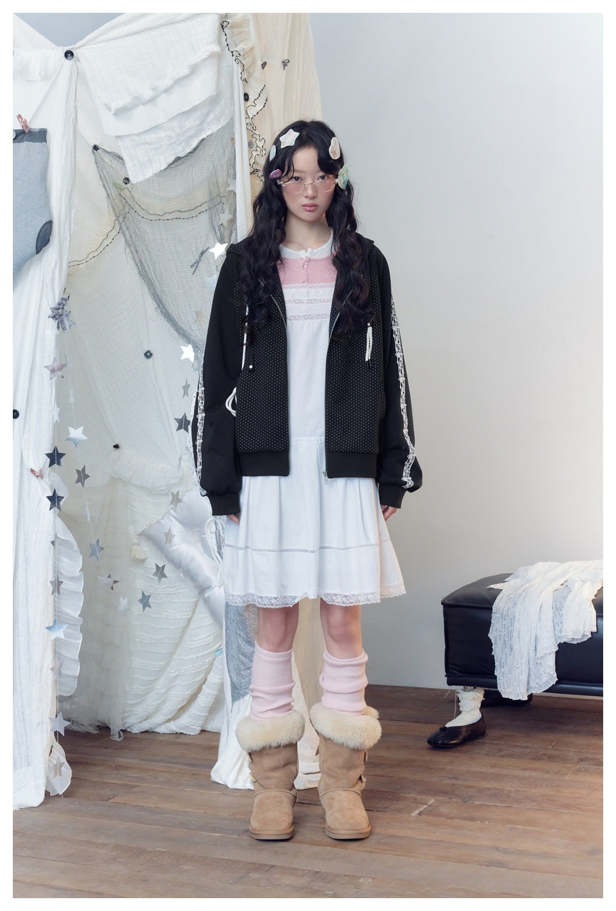 Full-length model wearing a black dotted zip hoodie with white sleeve graphics over a white knee-length dress.