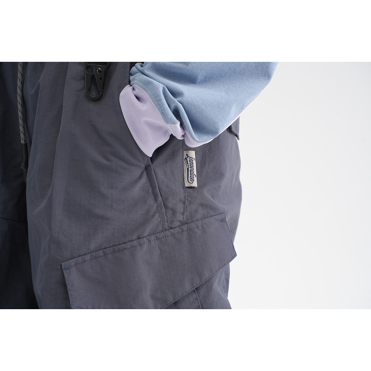 Close-up of dark charcoal cargo trousers with a large flap pocket and small side label; blue and lilac fabric overlaps the