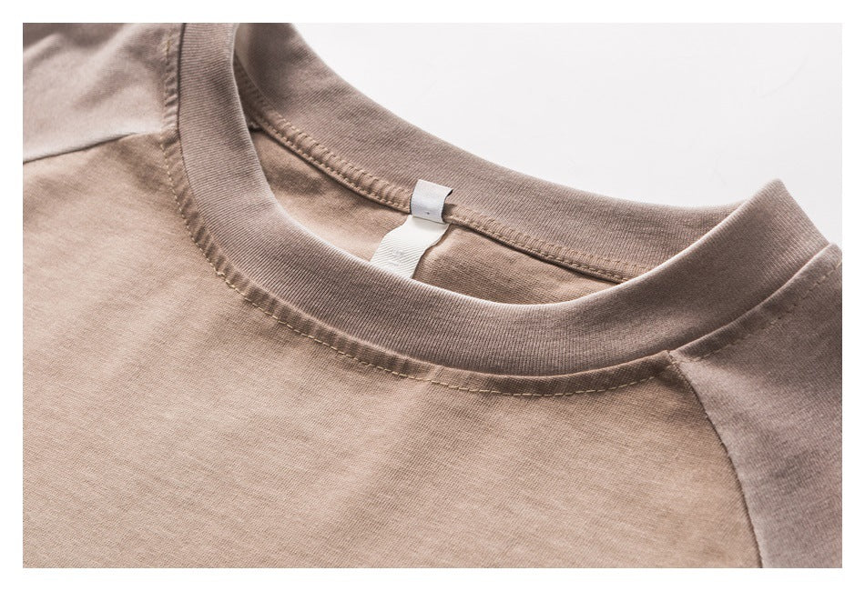 Close-up of a taupe T-shirt's ribbed crew neckline, shoulder seams, and inner neck tag.