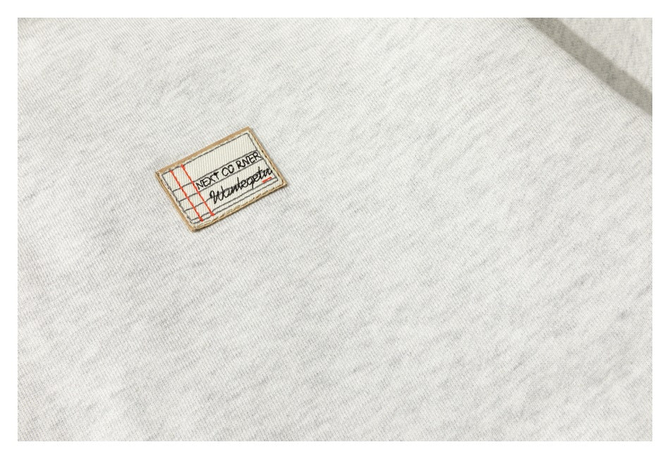 Small rectangular stitched patch with English lettering on light gray hoodie fabric.