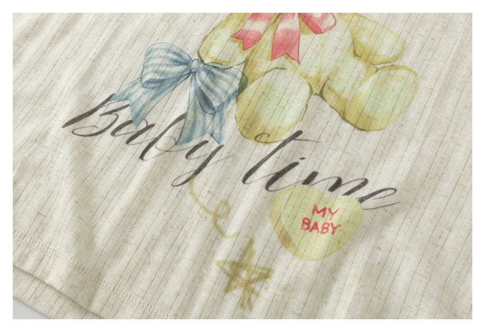 Close-up of cream textured fabric with a blue bow, pastel hearts, and English lettering printed on it.