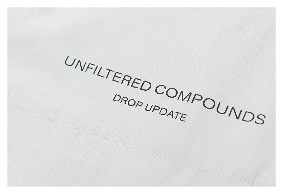 Close-up of pale gray garment fabric printed with “UNFILTERED COMPOUNDS” and “DROP UPDATE.”