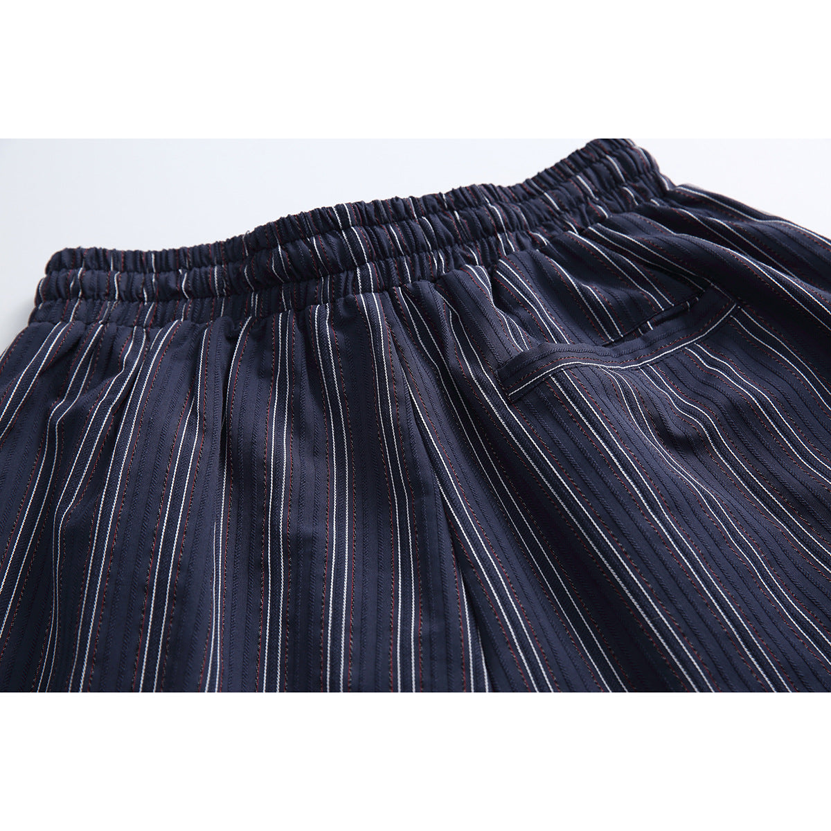 Close-up of navy pinstriped shorts showing the elastic waistband, drawstring, and a side pocket opening.