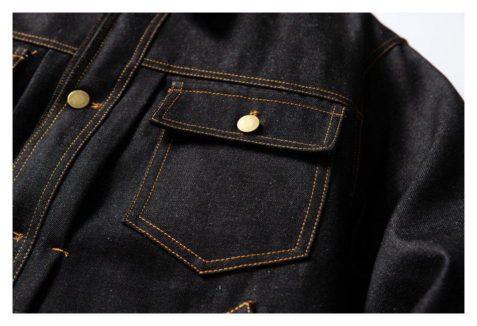 Close-up of a black denim jacket chest pocket with a button flap and contrasting golden-brown stitching.