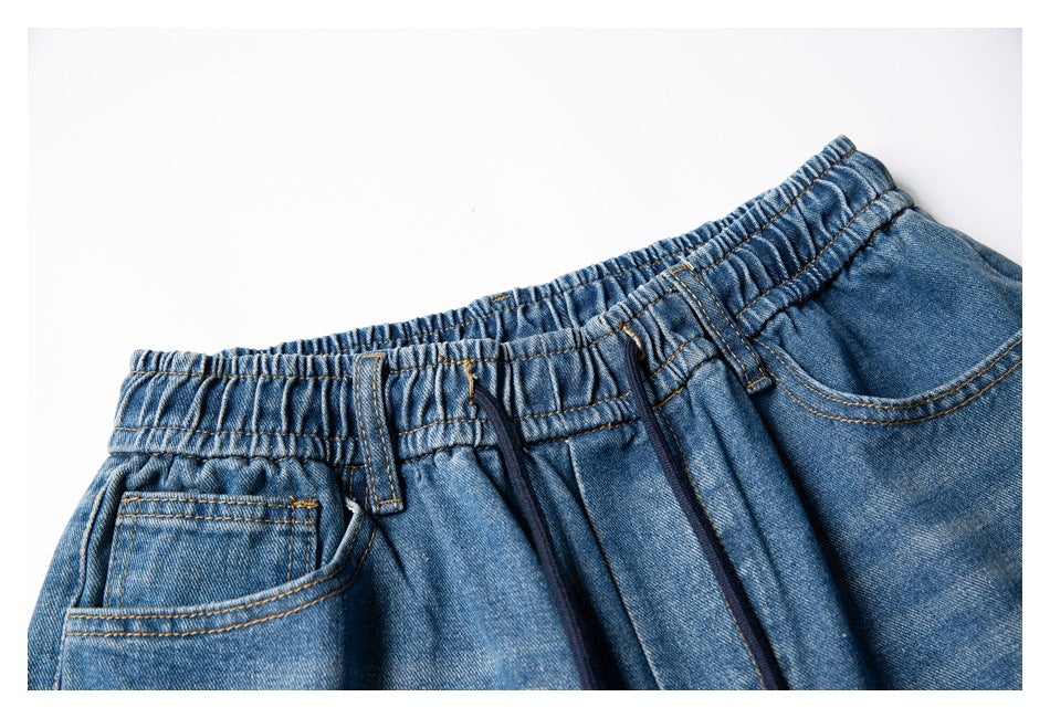 Close-up of blue denim pants with an elastic waistband, drawstring, belt loops, and front pockets.