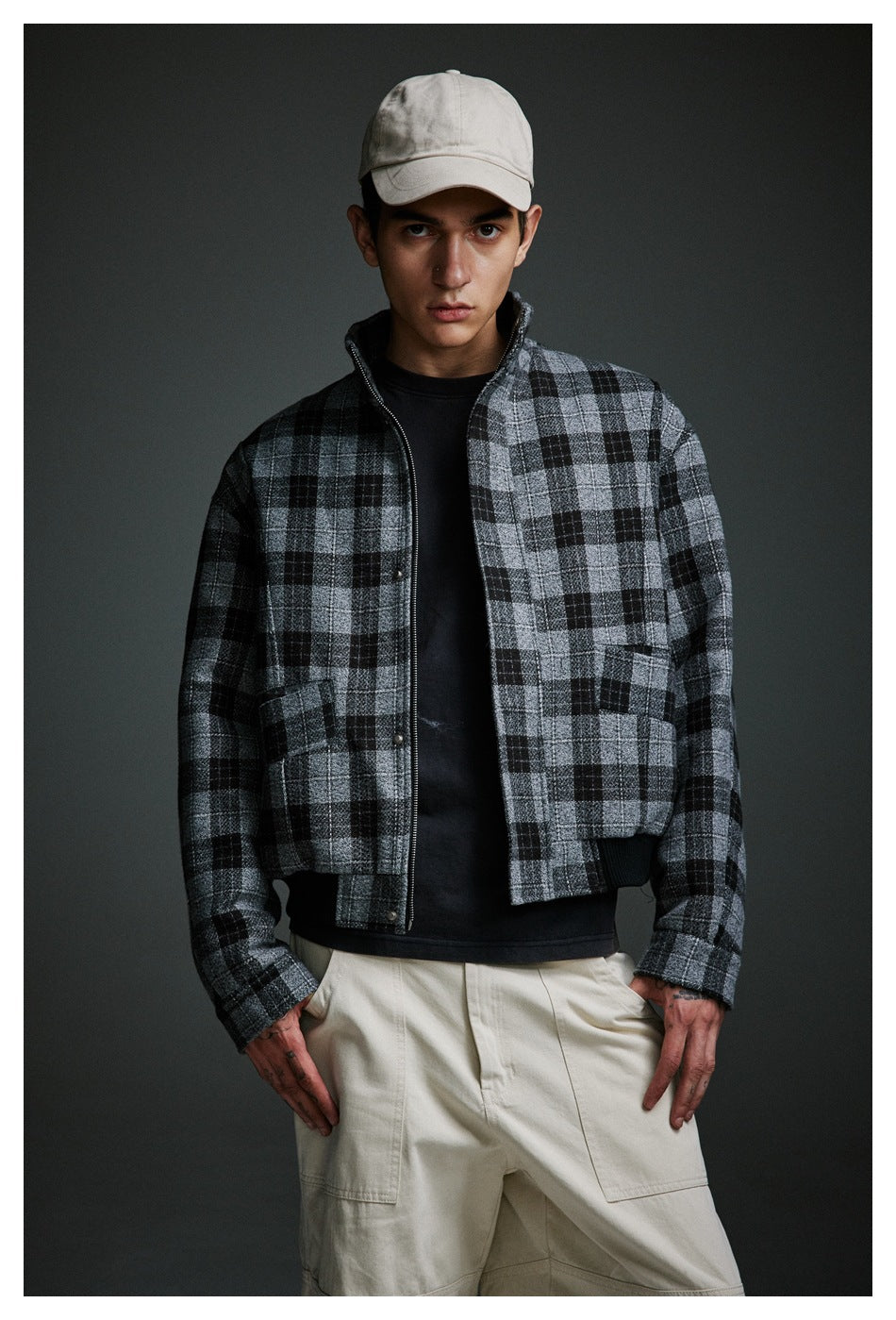 Close-up of a model in an open black and gray plaid jacket with stand collar, flap pockets and ribbed hem