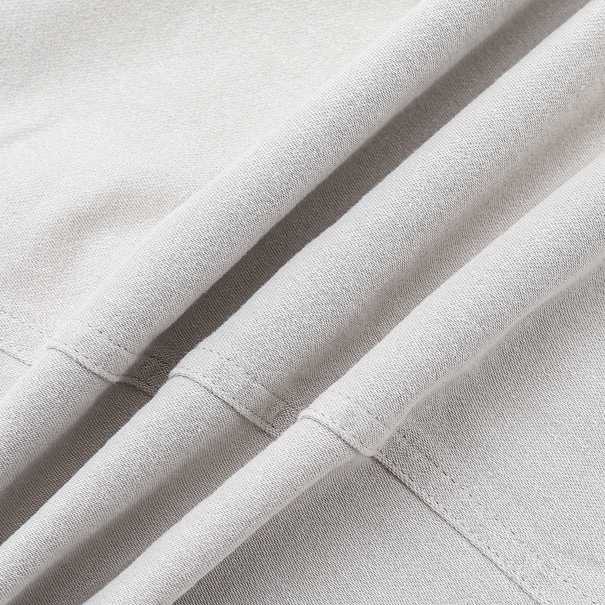 Close-up of light gray trouser fabric with folds and visible stitching.