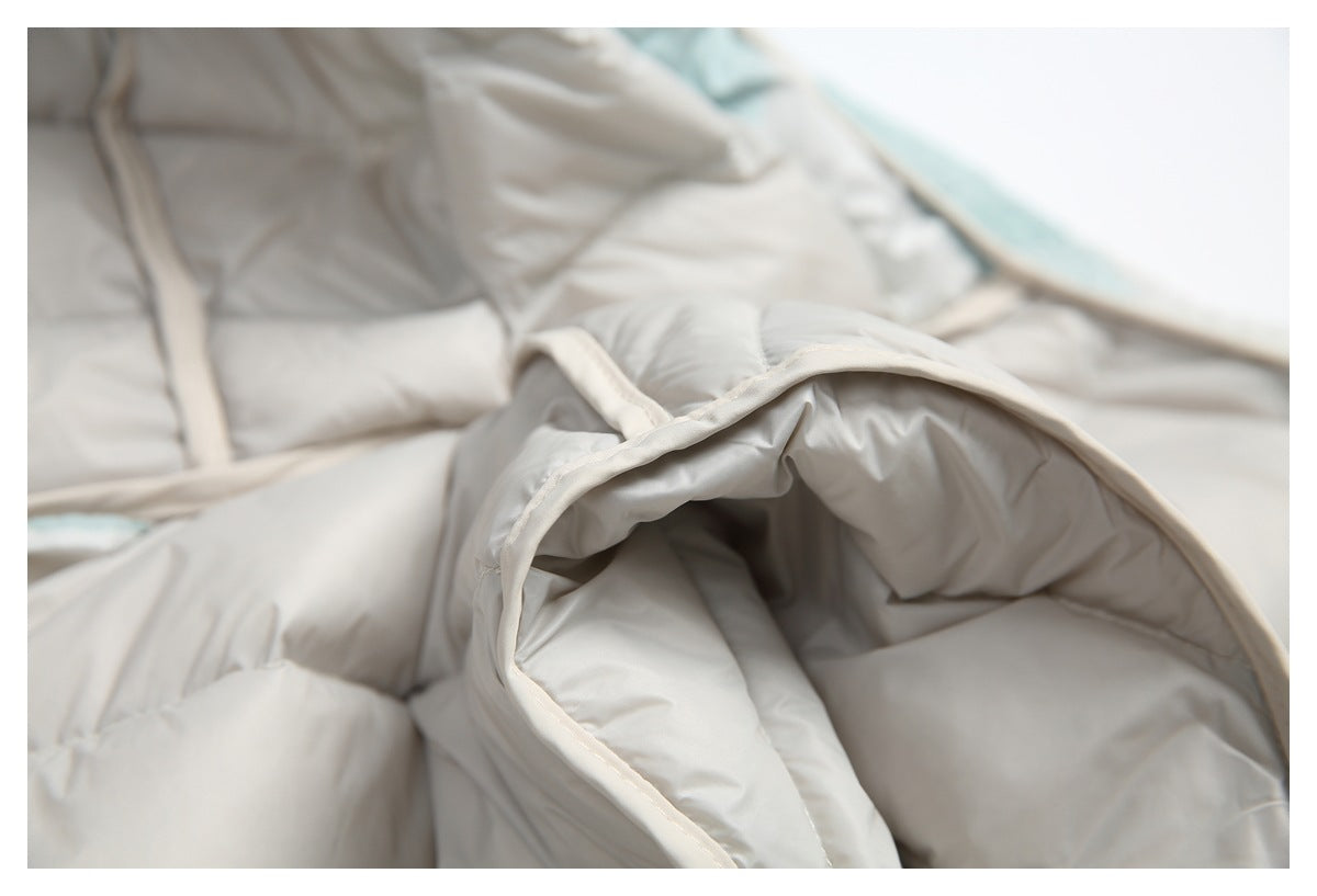 Close-up of a padded pale gray jacket section with curved cream-colored binding and quilted seams.
