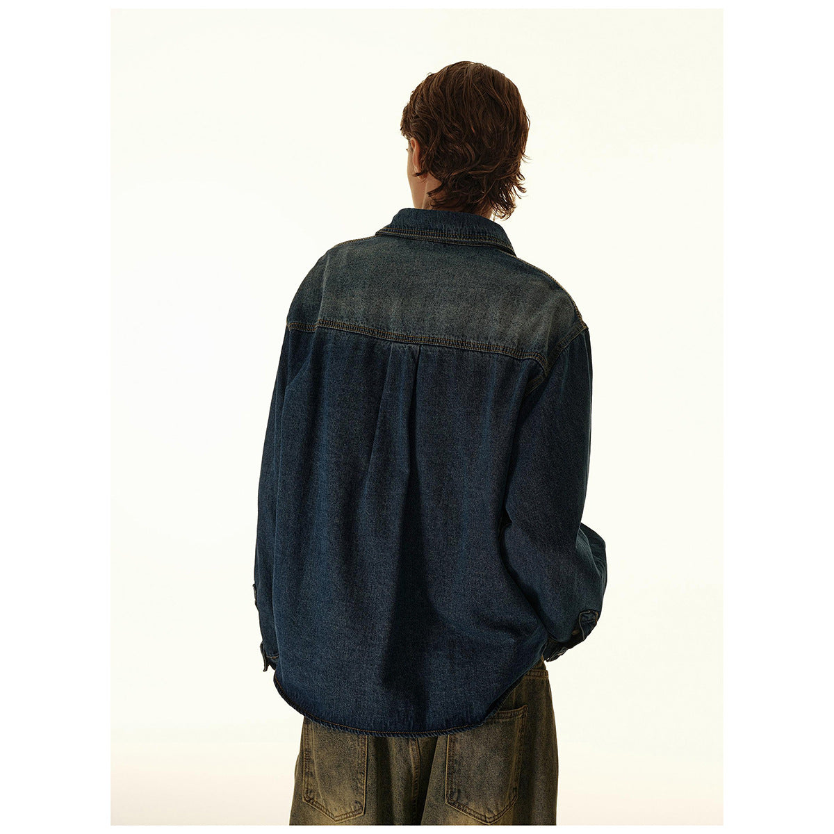 Rear view of a man wearing a dark blue denim overshirt with a yoke seam and curved hem.