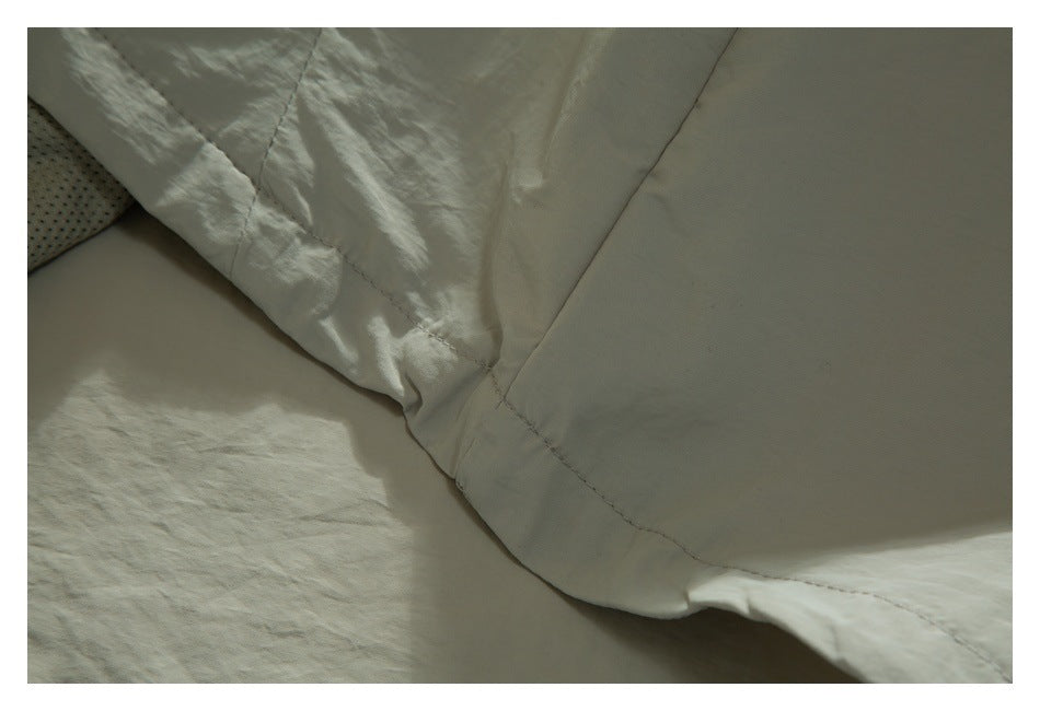 Close-up of pale sage garment fabric showing a stitched seam and a section of smooth lining.