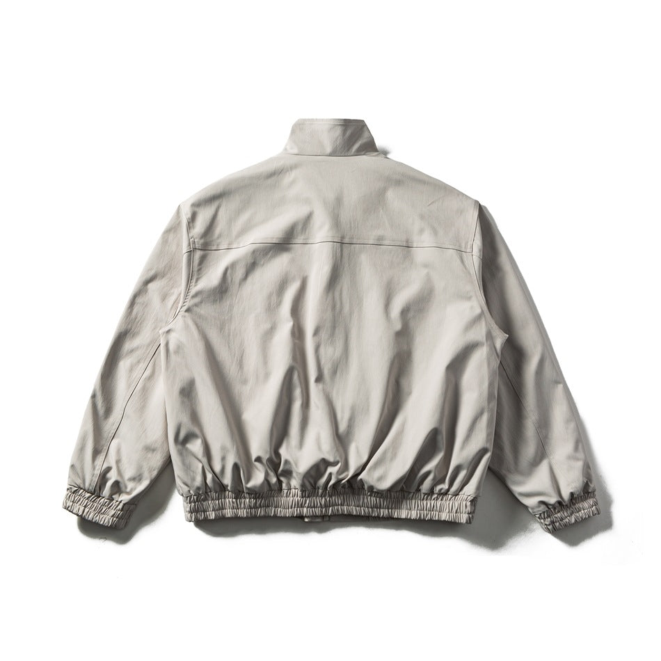 Back view of a light beige jacket with a stand collar, long sleeves, and gathered cuffs and hem.