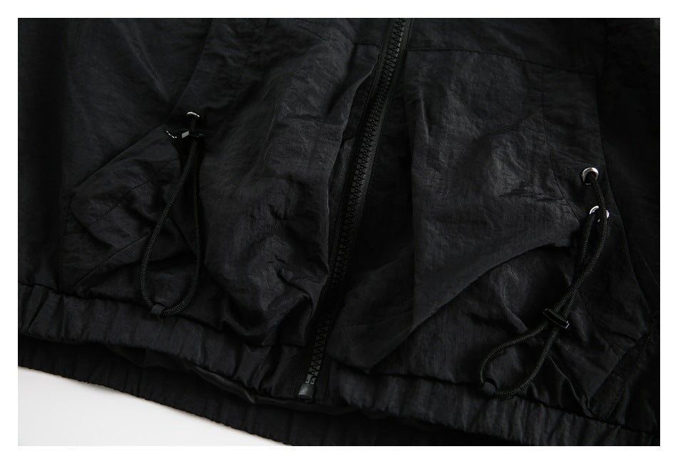 Close-up of a black garment front with a central zipper and two drawcord-adjusted pockets.