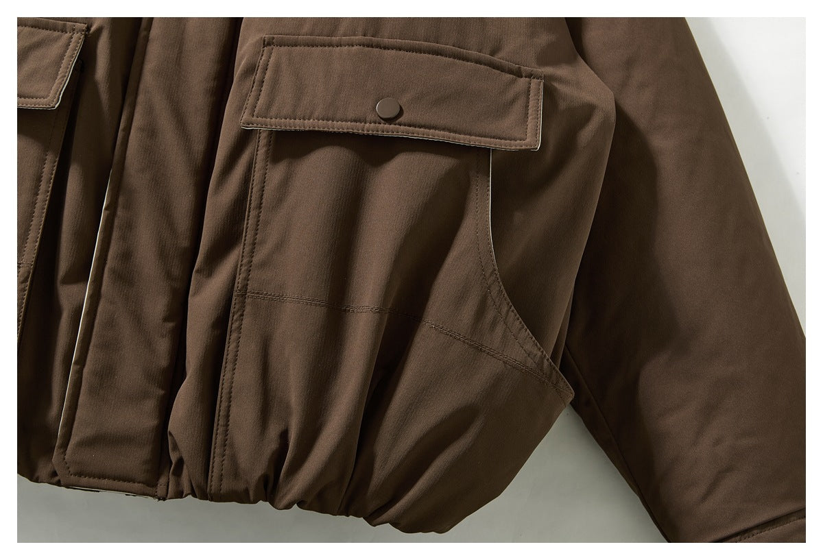 Close-up of a brown jacket's flap pocket with a snap button and curved seam near the elasticized hem.