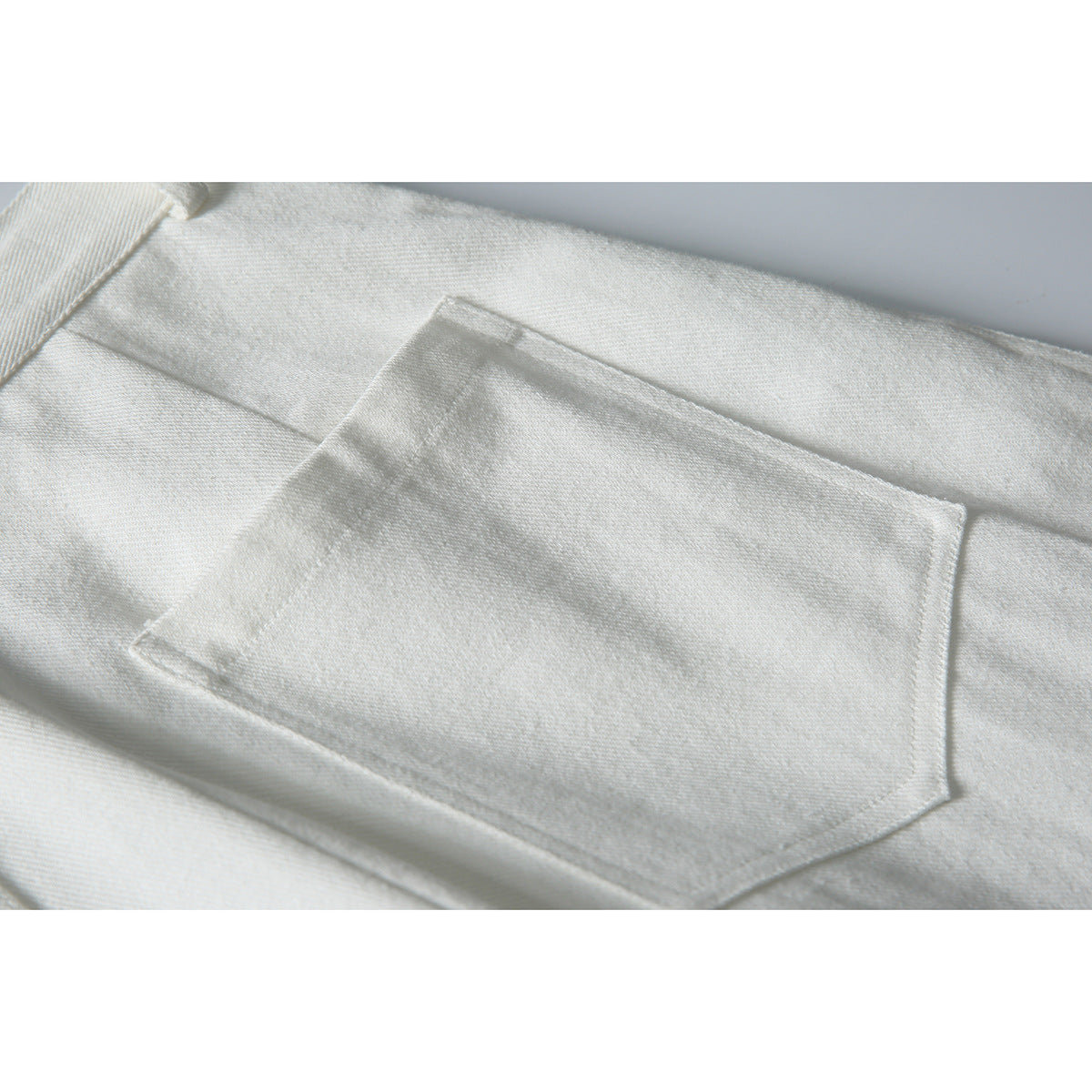 Close-up of a large stitched back pocket on white trousers.