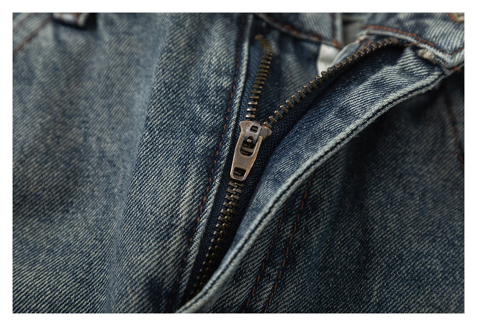 Close-up of the partially open metal zipper and fly on faded blue-gray jeans.