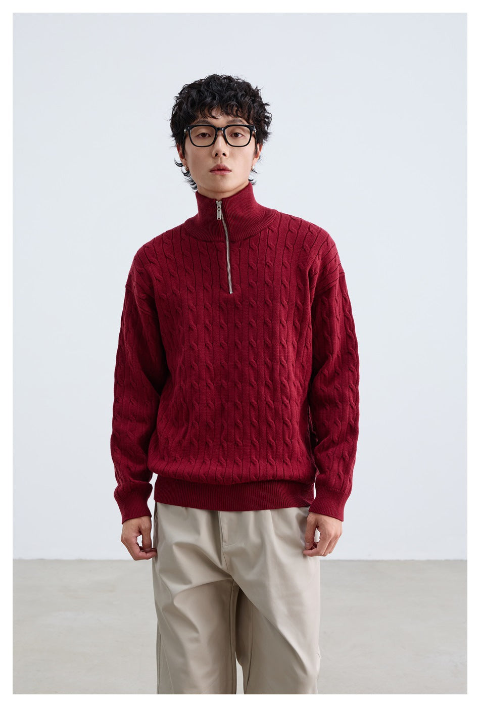 Man wearing a red cable-knit half-zip sweater with stand collar and beige trousers, front view