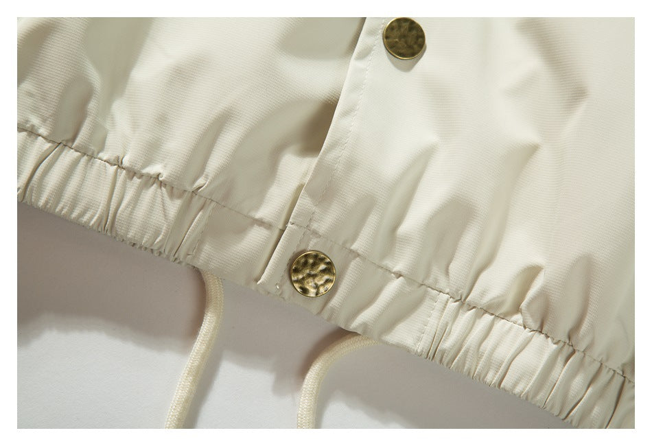 Close-up of an ivory garment’s gathered hem, drawcord, and gold-tone buttons.