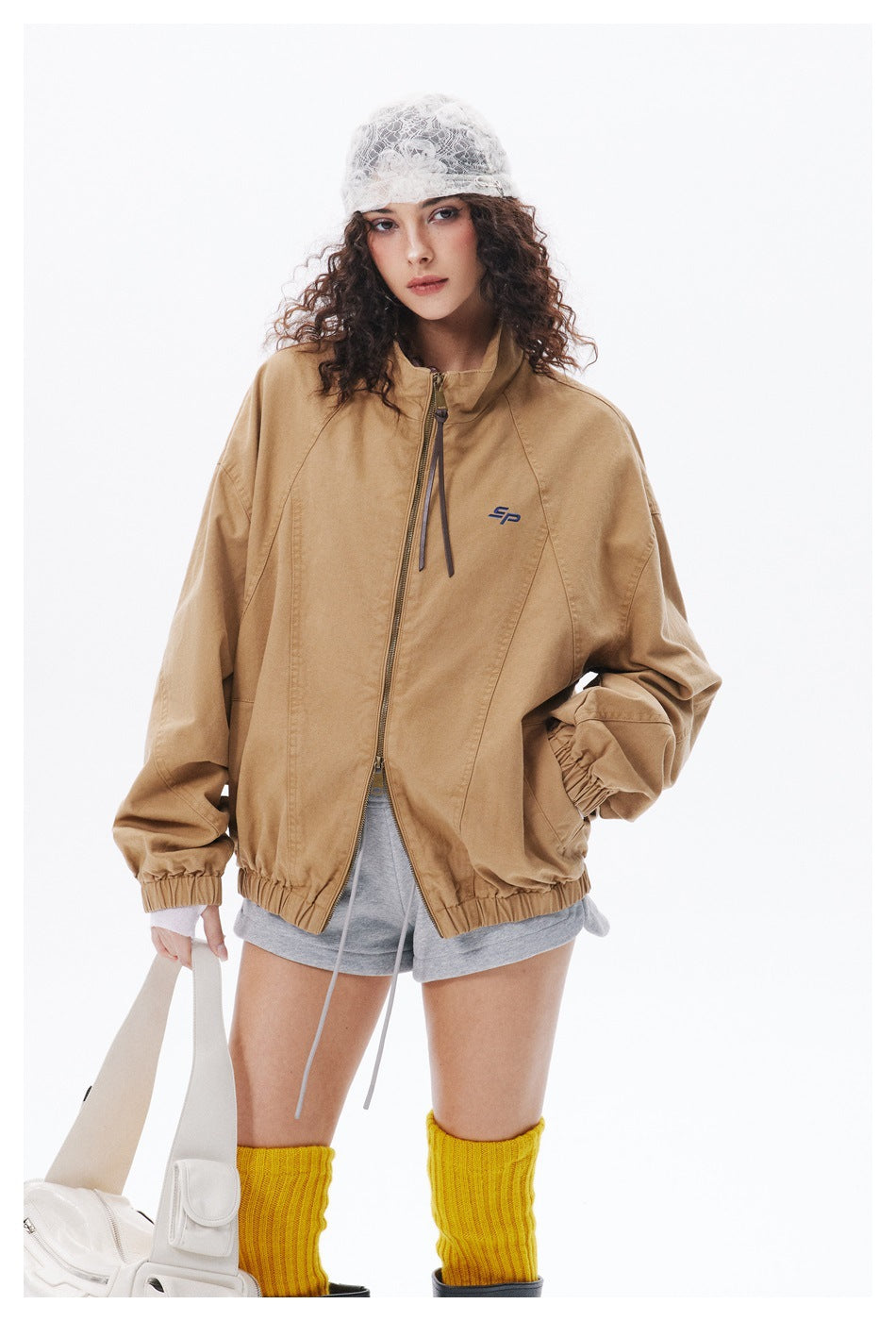 Model in a tan zip-front jacket with a stand collar, roomy sleeves, elastic cuffs, and a small chest emblem.