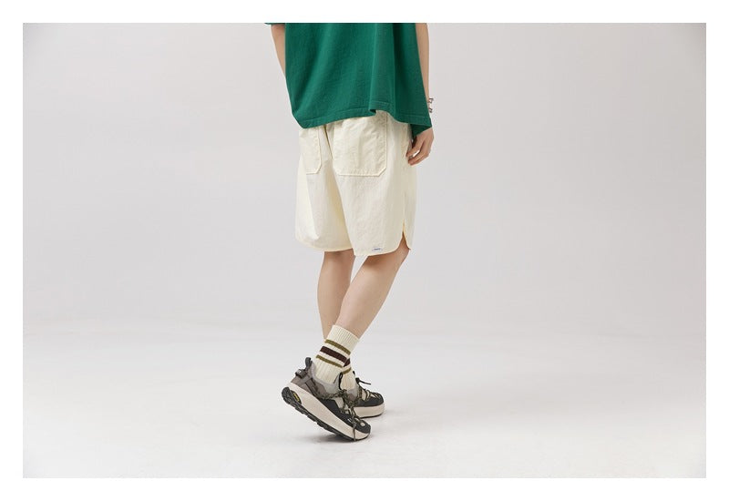 Angled rear view of a model wearing off-white knee-length shorts with large patch pockets.