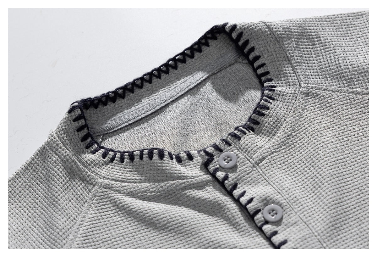 Close-up of a light gray textured shirt neckline with dark contrast stitching and two pale buttons.