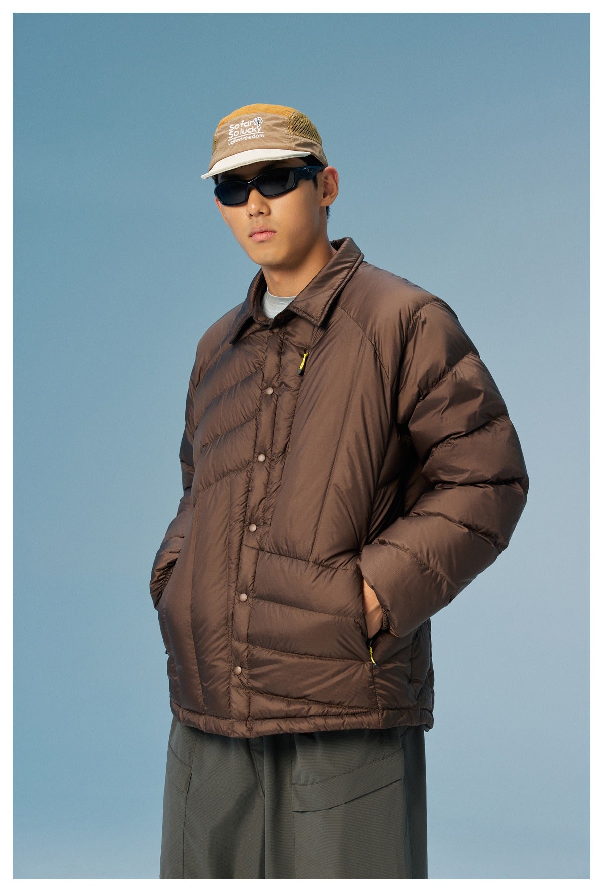 Model wearing a dark brown quilted jacket with a pointed collar, snap front, and yellow zipper pulls.
